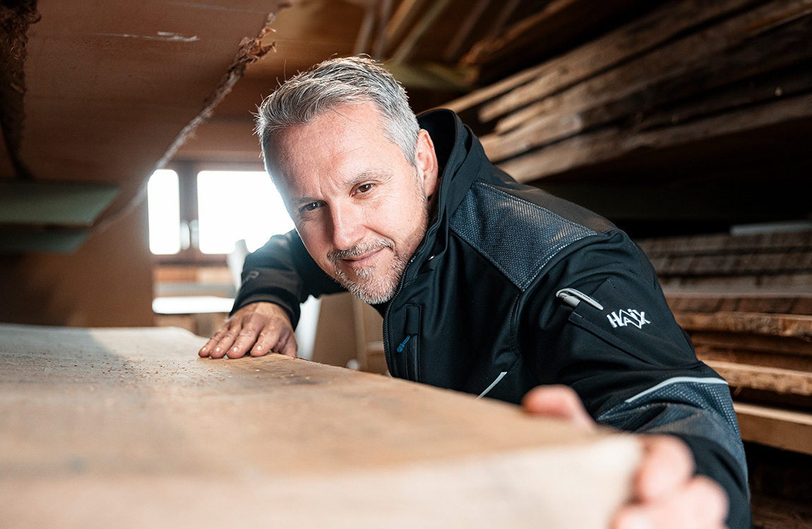 Holzbearbeitung, Arbeitsjacke, Holzstapel, Mann, Arbeitshaltung, Arbeitskleidung, Mantel, Reißverschlussfach, graue Haare, Holzbearbeitung